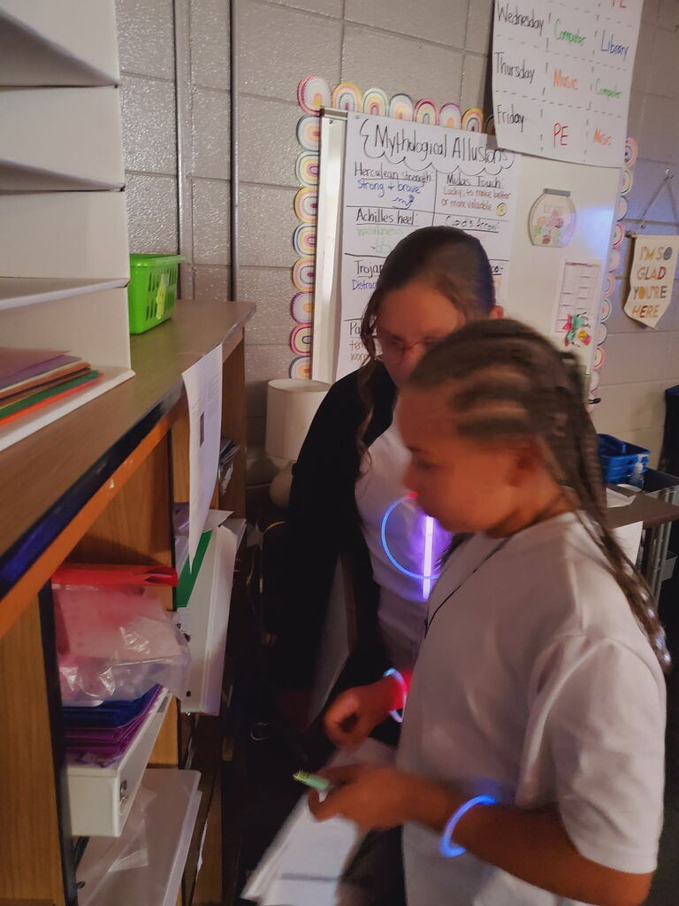 Two students examine a project in a classroom. One looks at a tablet while the other looks down.