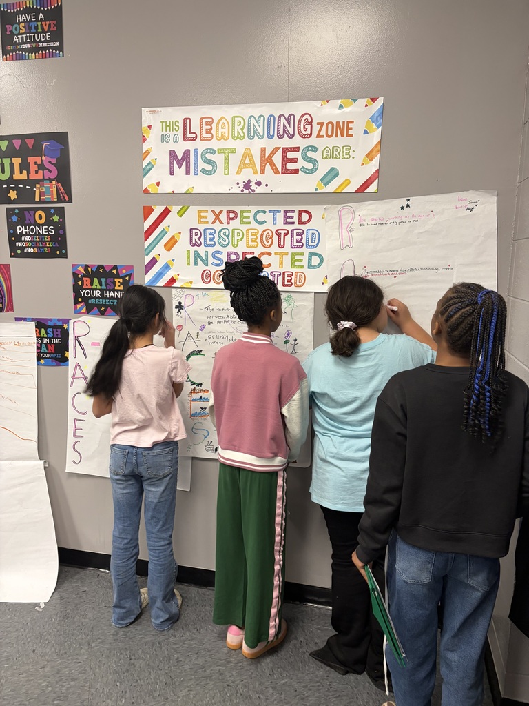 Five children examine posters on a wall. One poster reads "Learning Zone Mistakes." A few are writing on paper.