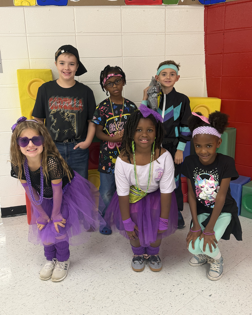 Six children in costumes pose together for a photo in front of colorful building blocks.