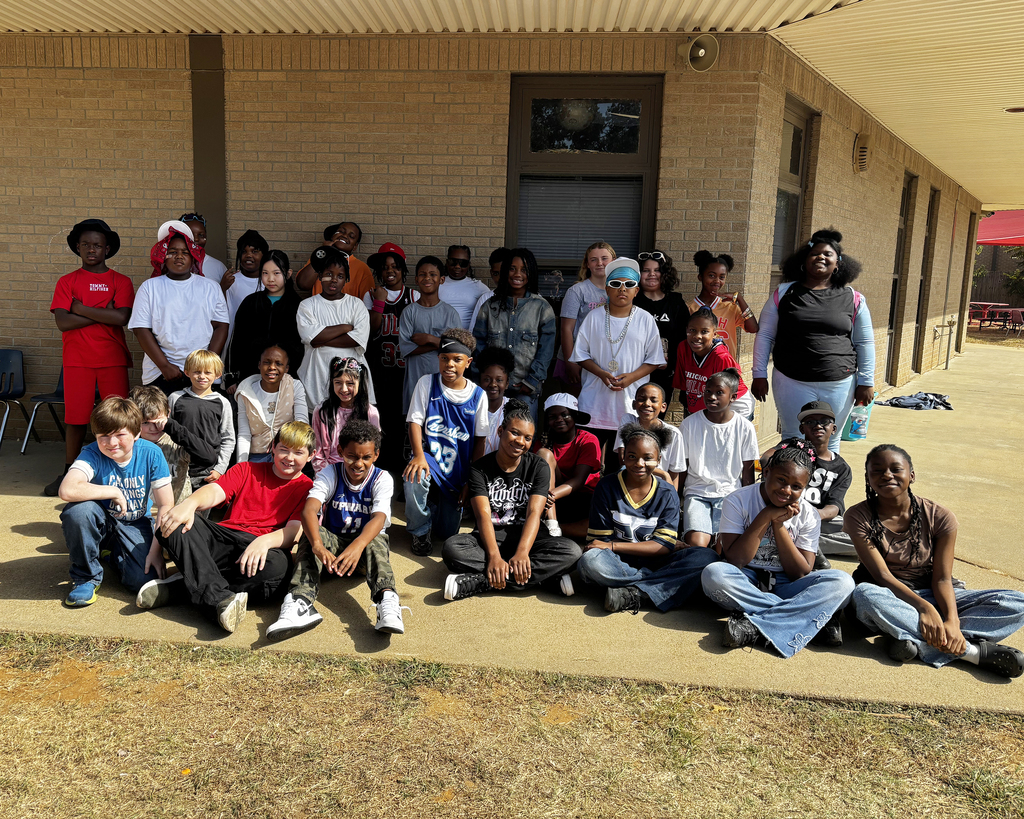 A group of people sitting and standing in front of a building. Some are wearing sneakers.