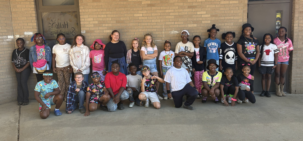 Group of young people, including adults, stand and crouch in front of a brick wall.