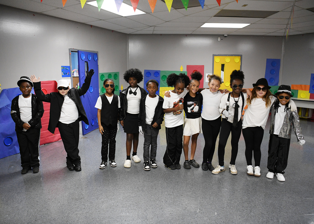 A group of kids in coordinated outfits stand in a room with colorful Lego blocks in the background.