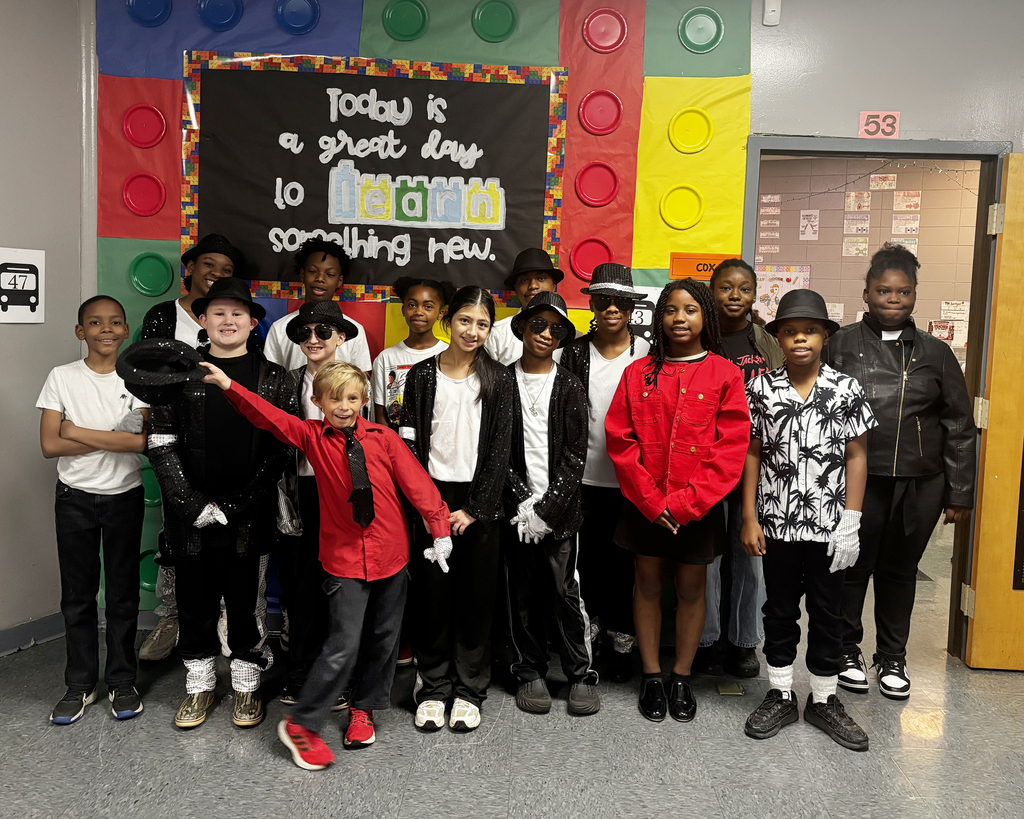 Group of children wearing matching costumes standing in front of a colorful Lego wall.