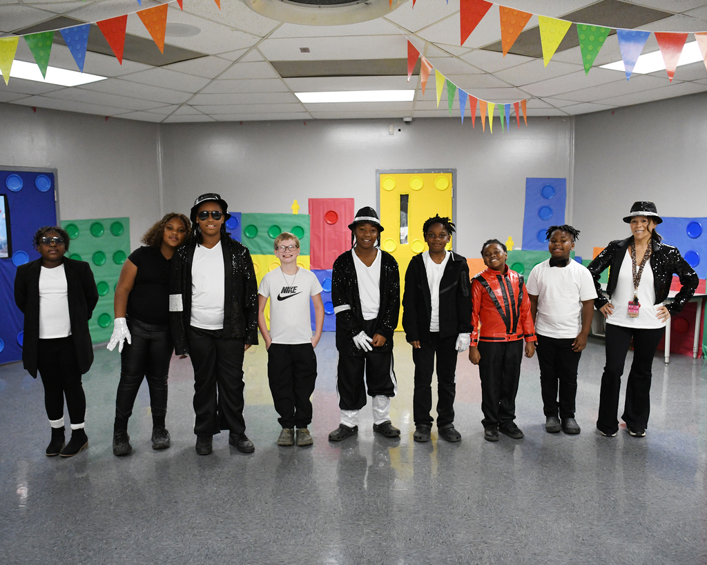 A group of students wearing Michael Jackson-themed costumes standing in a room with a Lego wall.
