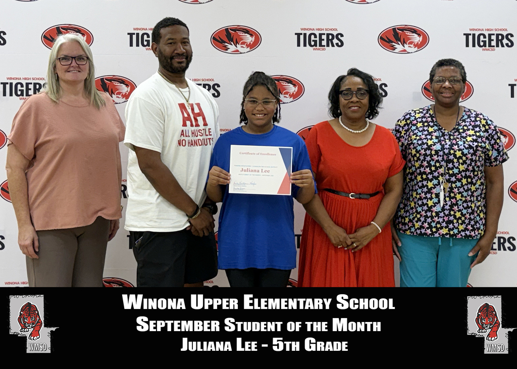 Five adults and one child stand behind a white backdrop with "Tigers" and logos. Child holds a certificate. Text reads "Winona Upper Elementary School September Student of the Month."