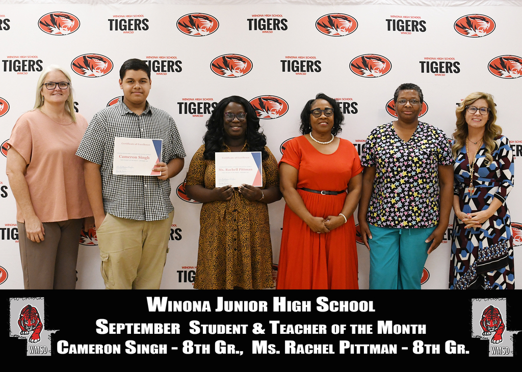 Five adults, including three women, stand for a photo, holding certificates. Behind them is a white backdrop with "Tigers" and "Winona Junior High School" text.