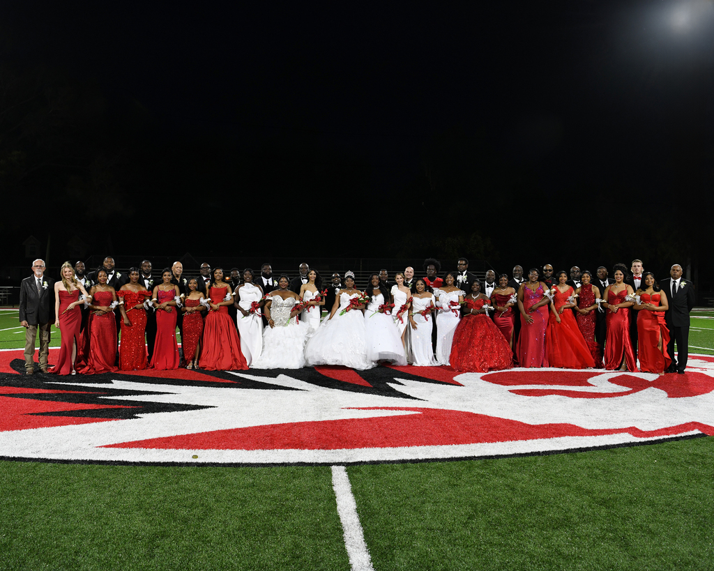 People in red and white clothing stand on a football field at night. A logo is on the field.