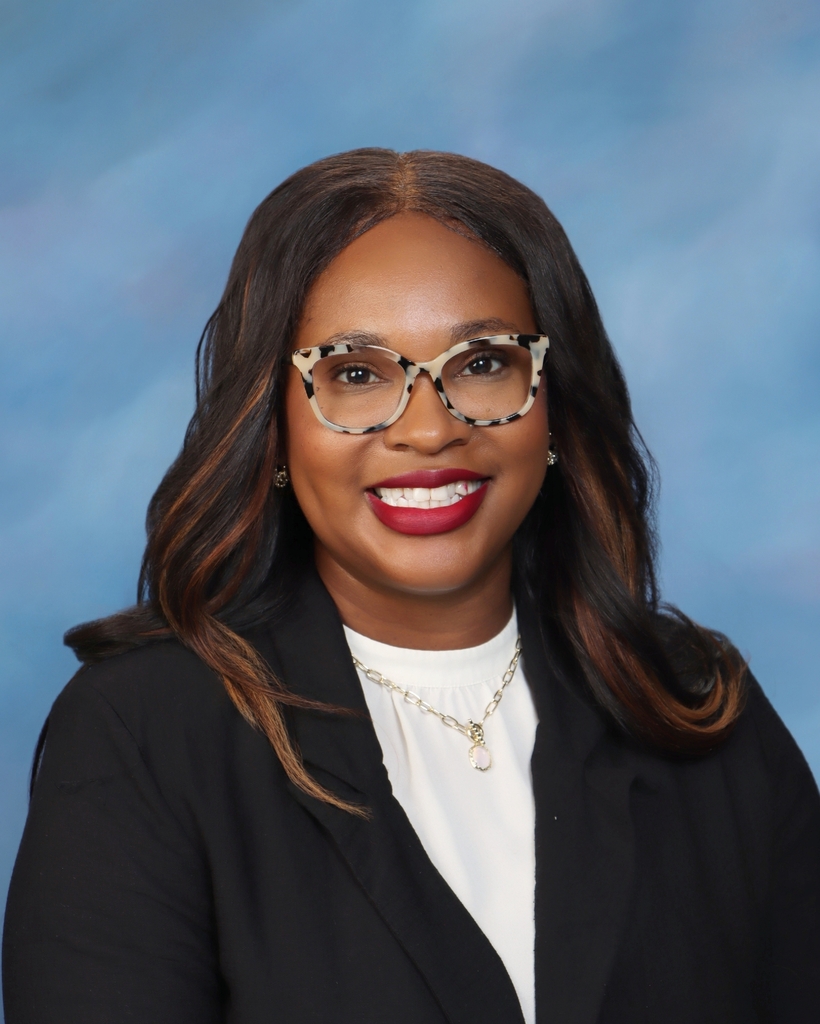 Person in glasses and a black blazer poses with a smile against a blue background.
