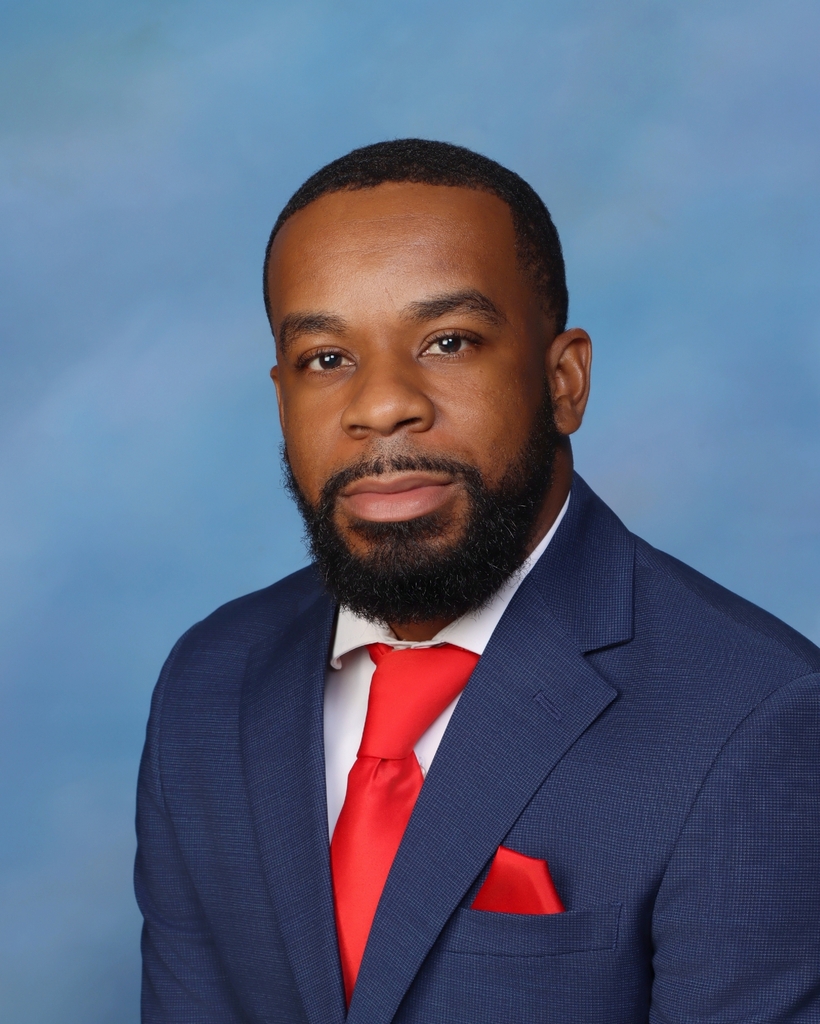 Man with short beard, wearing dark blue suit jacket, white shirt, and red tie. Red handkerchief in breast pocket.