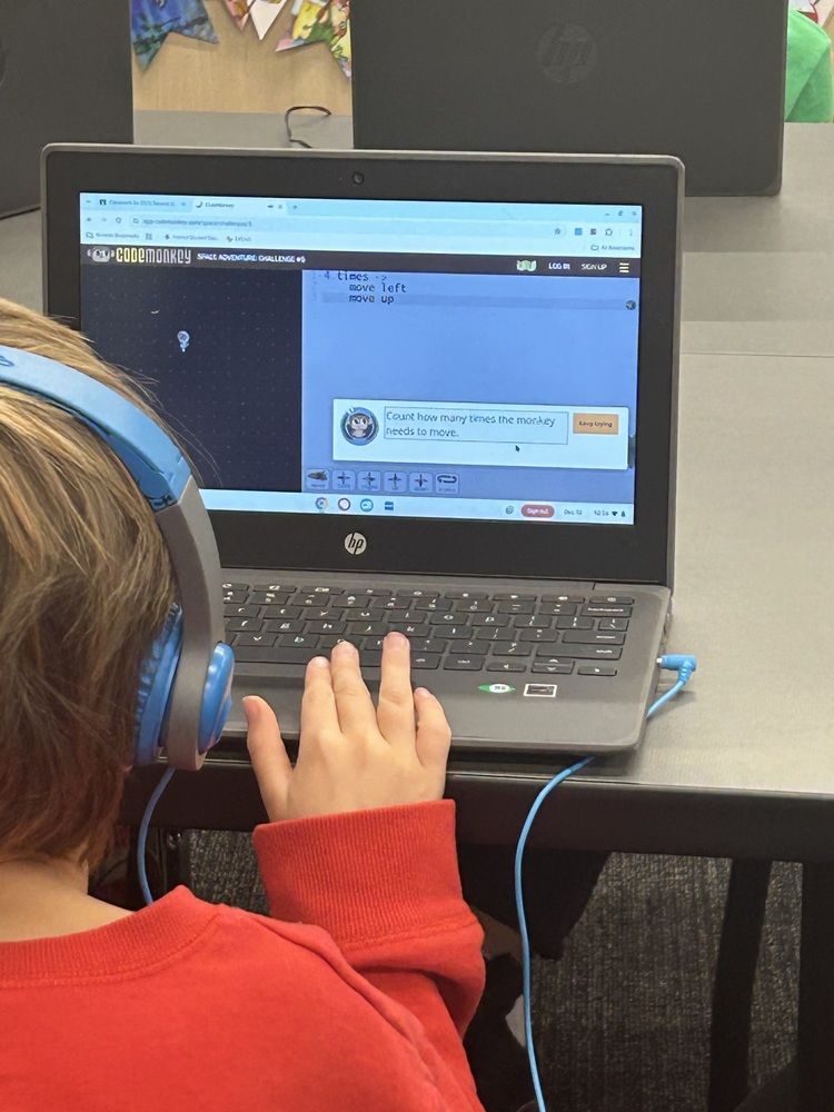 Here’s a shorter version:  **Alt text:** *A child with blue headphones uses a laptop showing a coding task that says, “Count how many times the monkey needs to move.”*