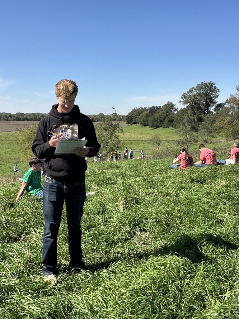 Student standing in a field studying Land Judging papers