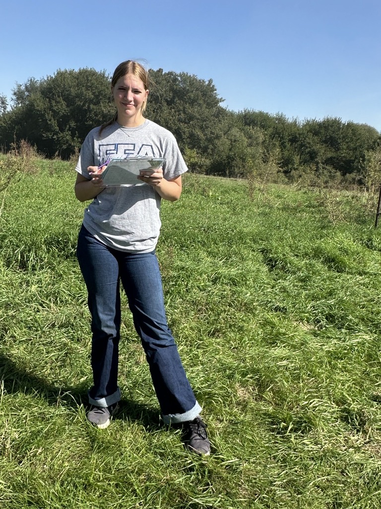 Student standing in a field studying Land Judging papers