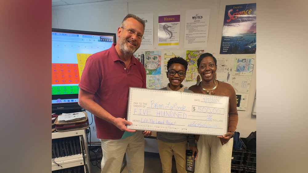 Hanes Middle School student presenting a school supply check to teacher at the school