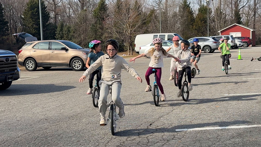 Unicycle students riding in a line through school parking lot