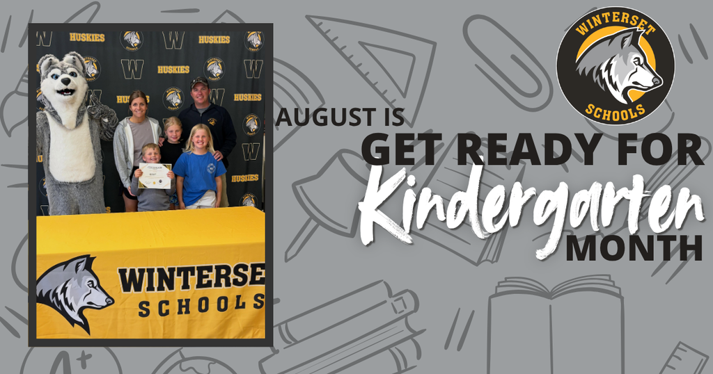 A group stands in front of a sign with the words "August is Get Ready for Kindergarten Month".