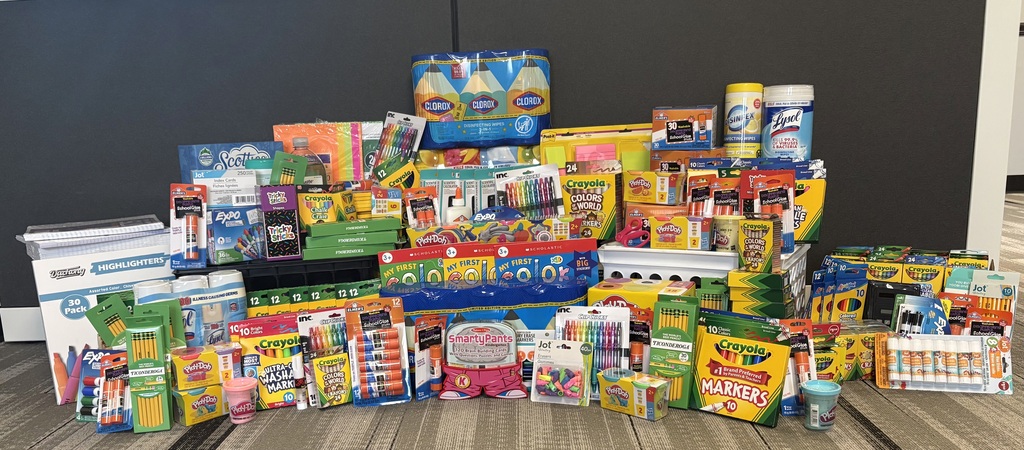 A variety of colorful school supplies are arranged in a pile on a floor