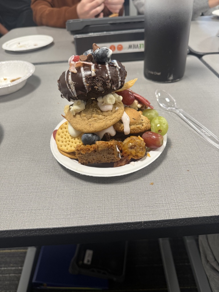 A plate with a layered dessert and fruits on a table with a cup and spoon.