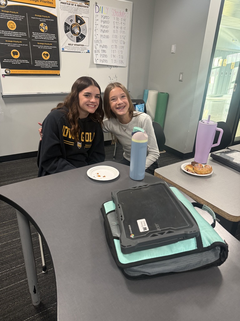 Two girls sitting at a table with a plate, a bottle, a bag, and a cup.