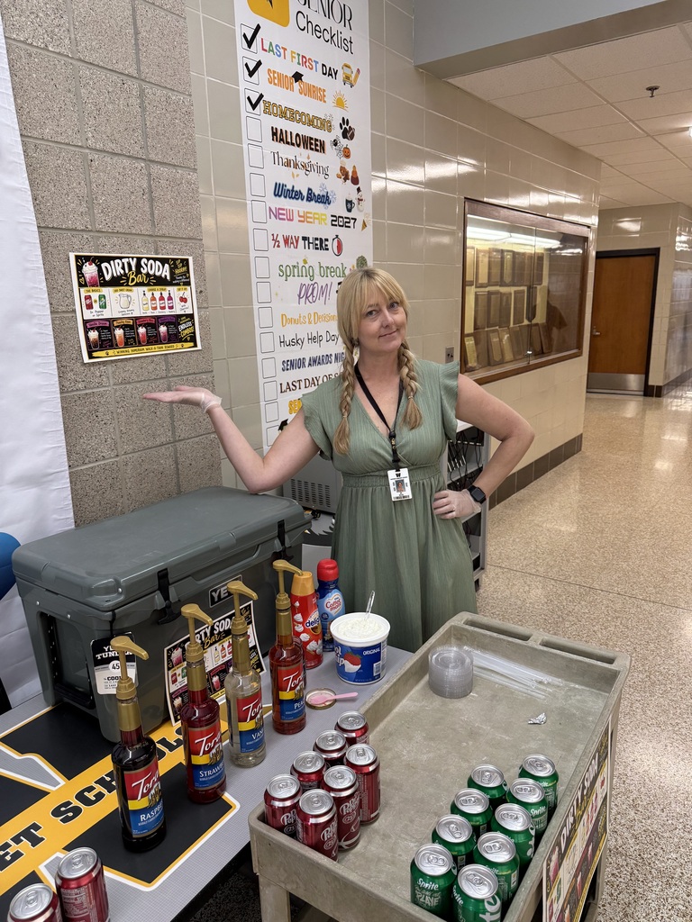Woman in green dress standing in hallway with table of condiments and cans of soda.