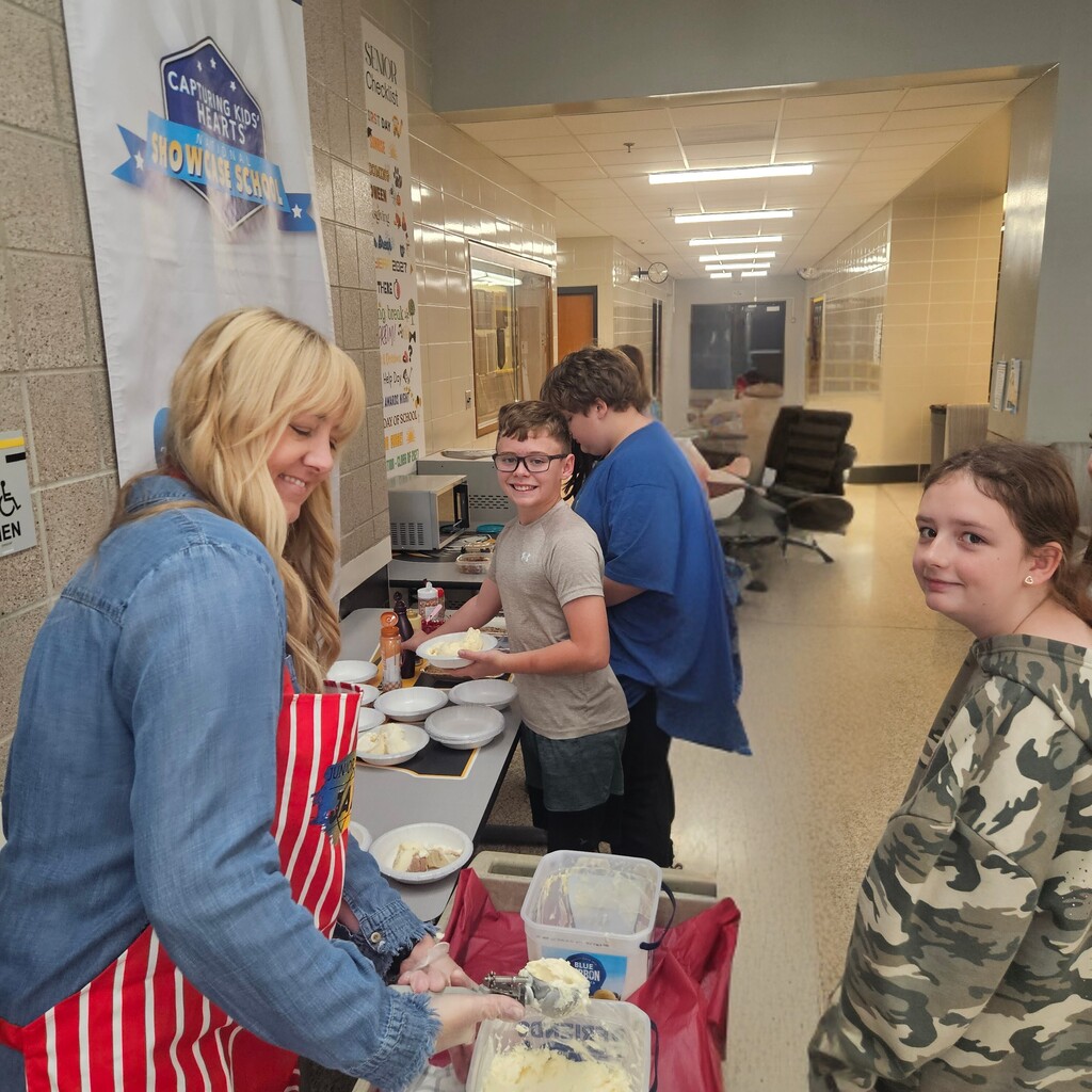 Four people in a kitchen area. One woman wears a blue apron. Three people are preparing food.
