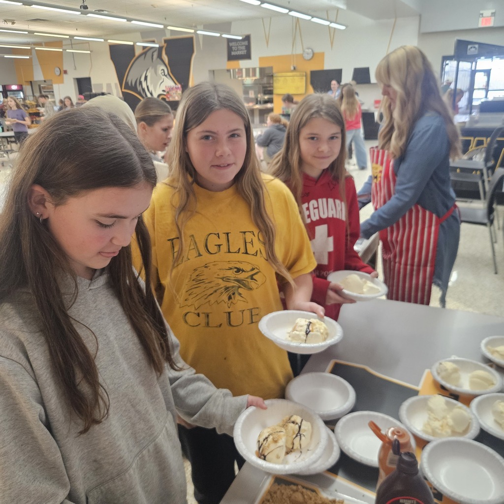 Several students gather around a table with plates of food. Two hold plates, and another holds a bowl.