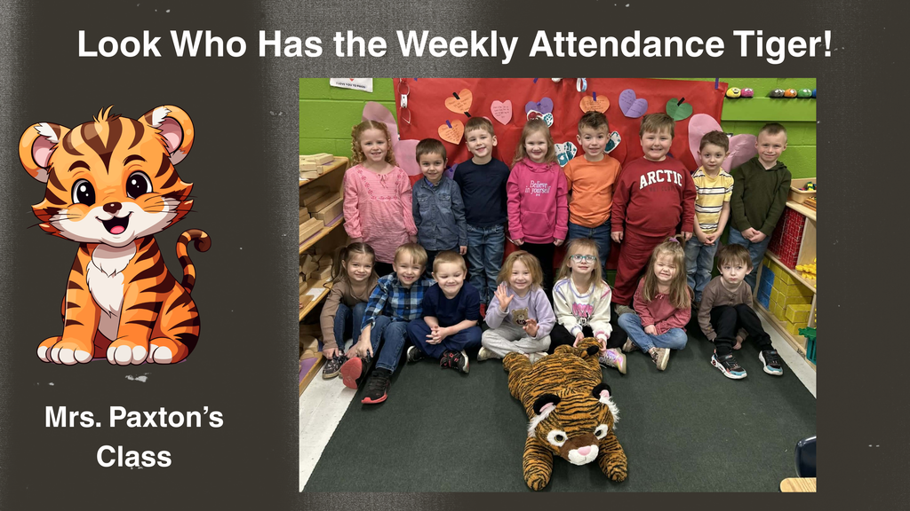A classroom group photo shows students from Ms. Paxton’s class standing and sitting together in front of a red bulletin board decorated with multicolored paper hearts. A large plush tiger, known as the Attendance Tiger, is positioned on the floor in front of the group. The graphic includes an illustrated cartoon tiger on the left side with the text ‘Mrs. Paxton’s Class,’ and at the top the text reads, ‘Look Who Has the Weekly Attendance Tiger!’ The background includes classroom shelves and storage bins.