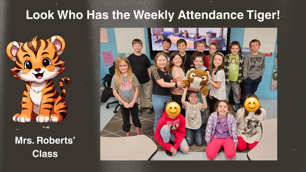 “A group of students from Mrs. Roberts’ class pose together inside a classroom. Several students stand and kneel in front of a bulletin board while holding a stuffed tiger mascot, known as the Attendance Tiger. A graphic on the left side of the image shows a cartoon tiger and text that reads, ‘Look Who Has the Weekly Attendance Tiger! Mrs. Roberts’ Class.’”