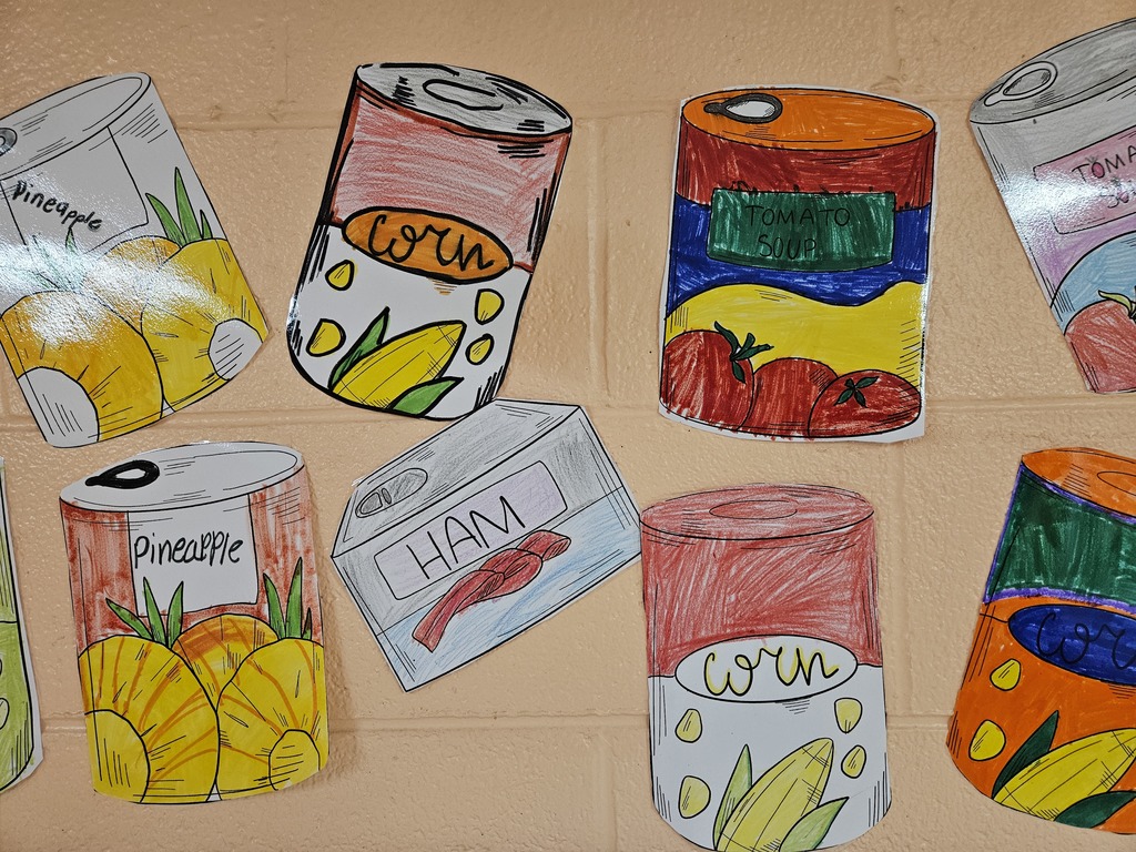 “Colorful, hand‑drawn paper cutouts of canned food displayed on a tan brick wall. The drawings include cans labeled pineapple, corn, tomato soup, ham, and blueberries, illustrated with bright colors and outlined details, representing a canned food drive.”