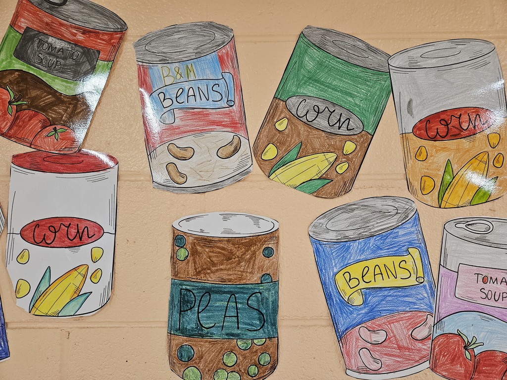 “Colorful, hand‑drawn paper cutouts of canned food displayed on a tan brick wall. The drawings include cans labeled pineapple, corn, tomato soup, ham, and blueberries, illustrated with bright colors and outlined details, representing a canned food drive.”