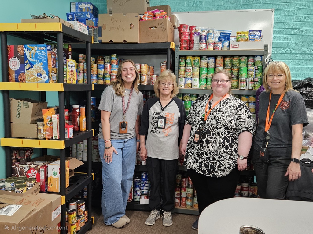 Five staff members stand in front of fully stocked pantry shelves filled with canned and boxed food items, recognizing their work counting, organizing, and preparing donations collected during the school food drive.