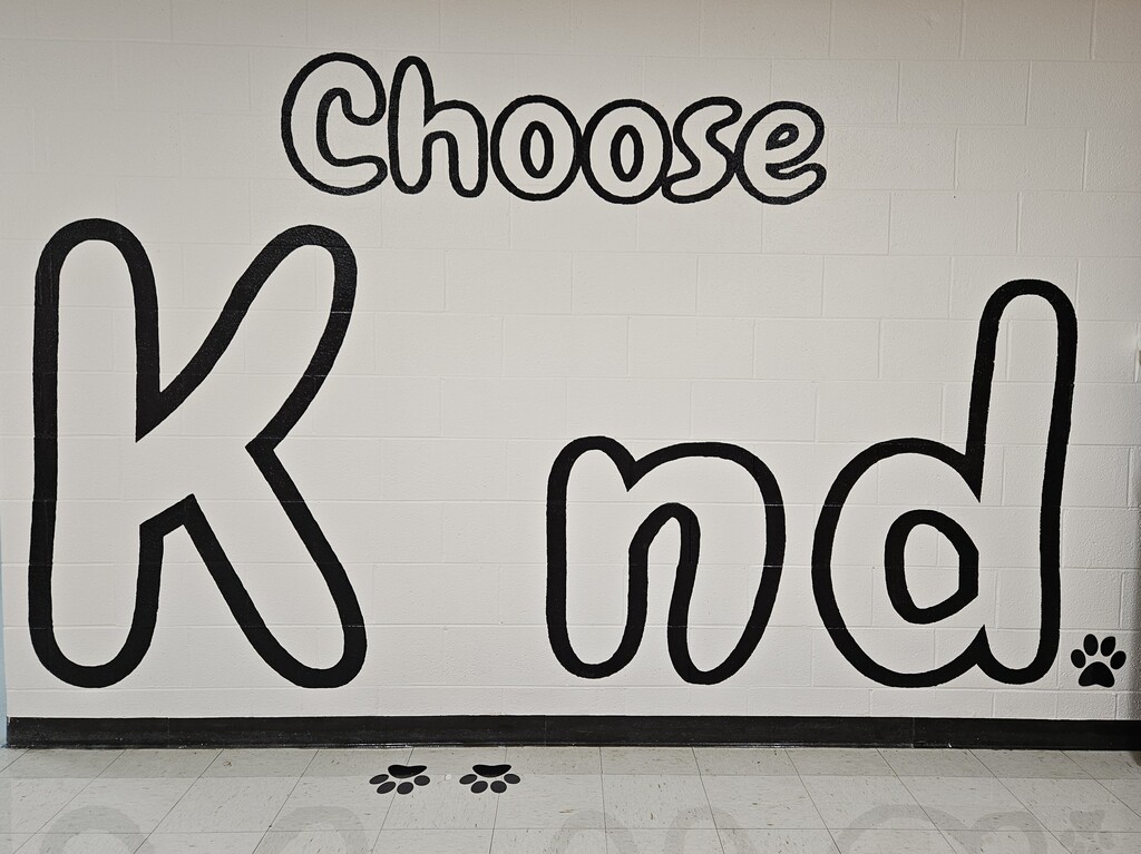 Photos inside Wirt County Primary Center showing new decorations added during the summer. Images include orange and black tiger paw prints painted on floors and walls, tiger-themed murals and artwork throughout the building, a "Choose K_nd" mural with the letter "i" intentionally omitted, and tiger images displayed in the cafeteria. The colorful decorations highlight Wirt County Tiger Pride and create an engaging environment for students returning for the new school year.