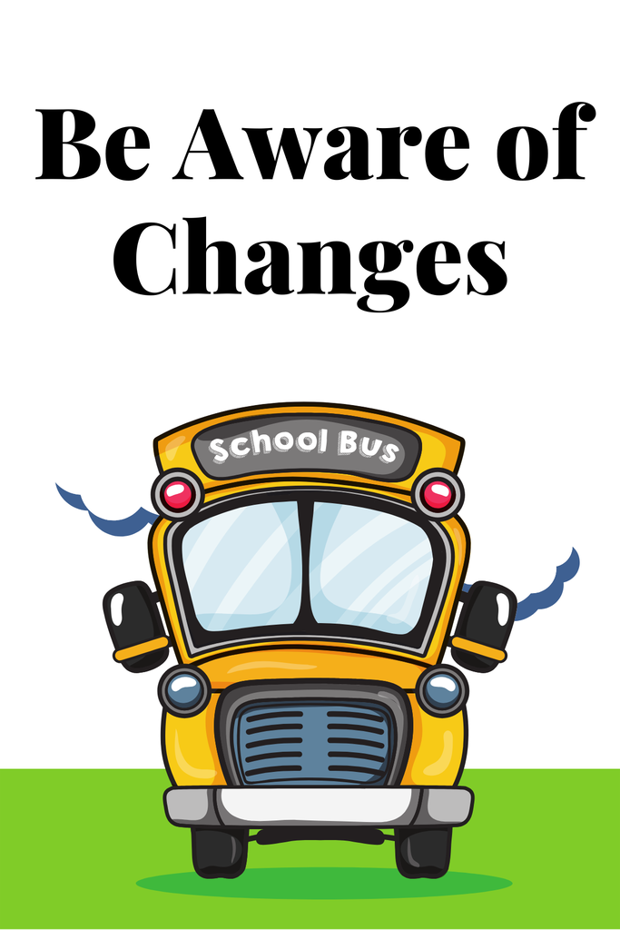 ADA-Compliant Alt Text: Graphic with the text “Be Aware of Changes” in large black letters at the top. Below the text is a front-facing cartoon yellow school bus with red lights, blue-tinted windows, black mirrors, and a gray bumper. The bus is centered on a light gray background with a green strip of grass at the bottom. Decorative blue cloud-like shapes appear behind the bus on both sides. The graphic serves as a notice that school transportation or operational changes are being announced.