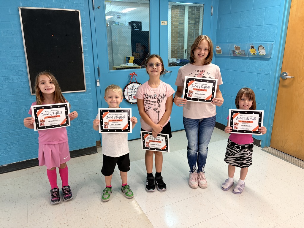 Five Wirt County Primary Center students stand in a school hallway holding August 2026 Student of the Month certificates. The students pictured represent the PreK, kindergarten, 1st grade, 3rd grade, and 4th grade recipients. Blue walls and classroom doors are visible in the background. The 2nd grade August Student of the Month, Sarah Arnold, is not pictured.