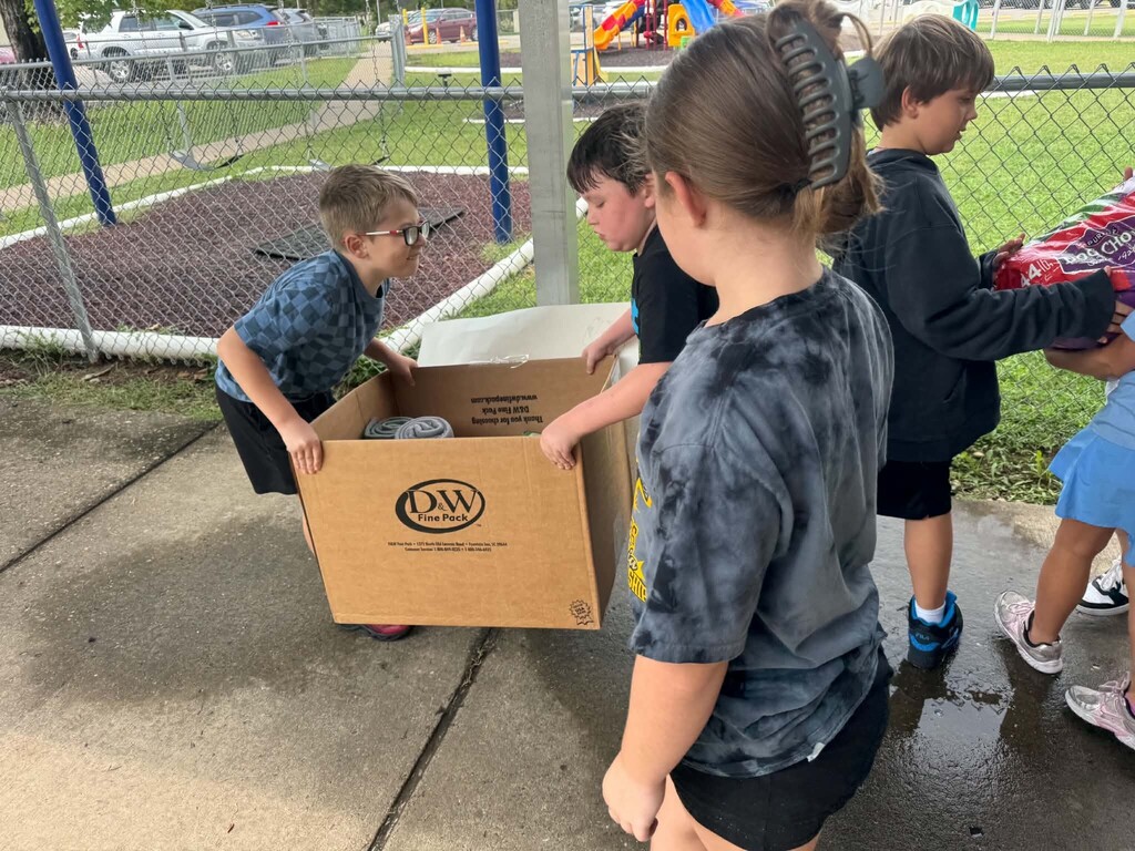 Mrs. Sims' class carrying boxes and bags of animal food and toy donations down the front sidewalk
