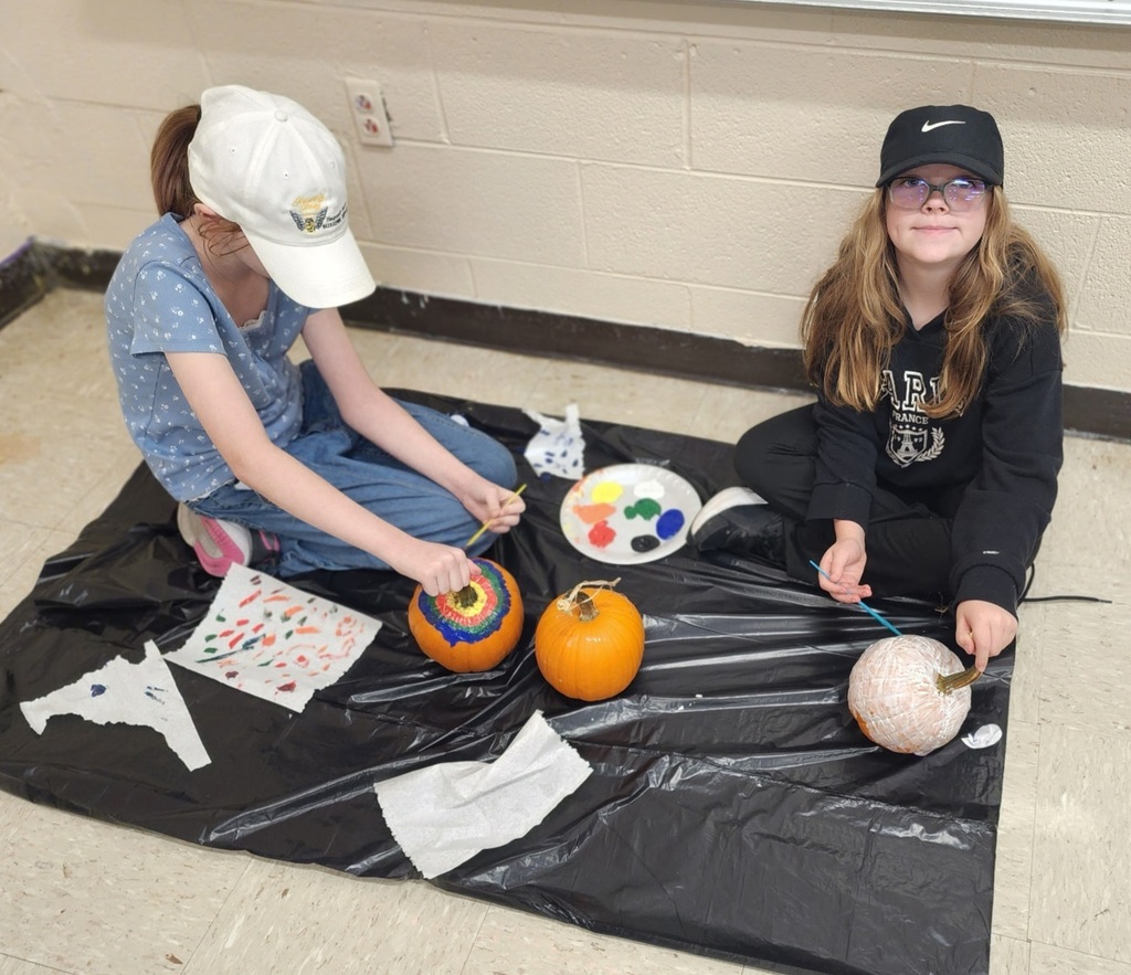 Photos show elementary students participating in a PBIS reward activity by painting pumpkins in various rooms throughout the school. Students use paint and art supplies to decorate pumpkins in different colors and designs while working at tables and classroom spaces. The pumpkins were provided by Moore’s Piggly Wiggly for students who earned enough PBIS points to participate in the fall activity.