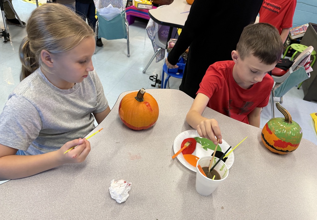 Photos show elementary students participating in a PBIS reward activity by painting pumpkins in various rooms throughout the school. Students use paint and art supplies to decorate pumpkins in different colors and designs while working at tables and classroom spaces. The pumpkins were provided by Moore’s Piggly Wiggly for students who earned enough PBIS points to participate in the fall activity.