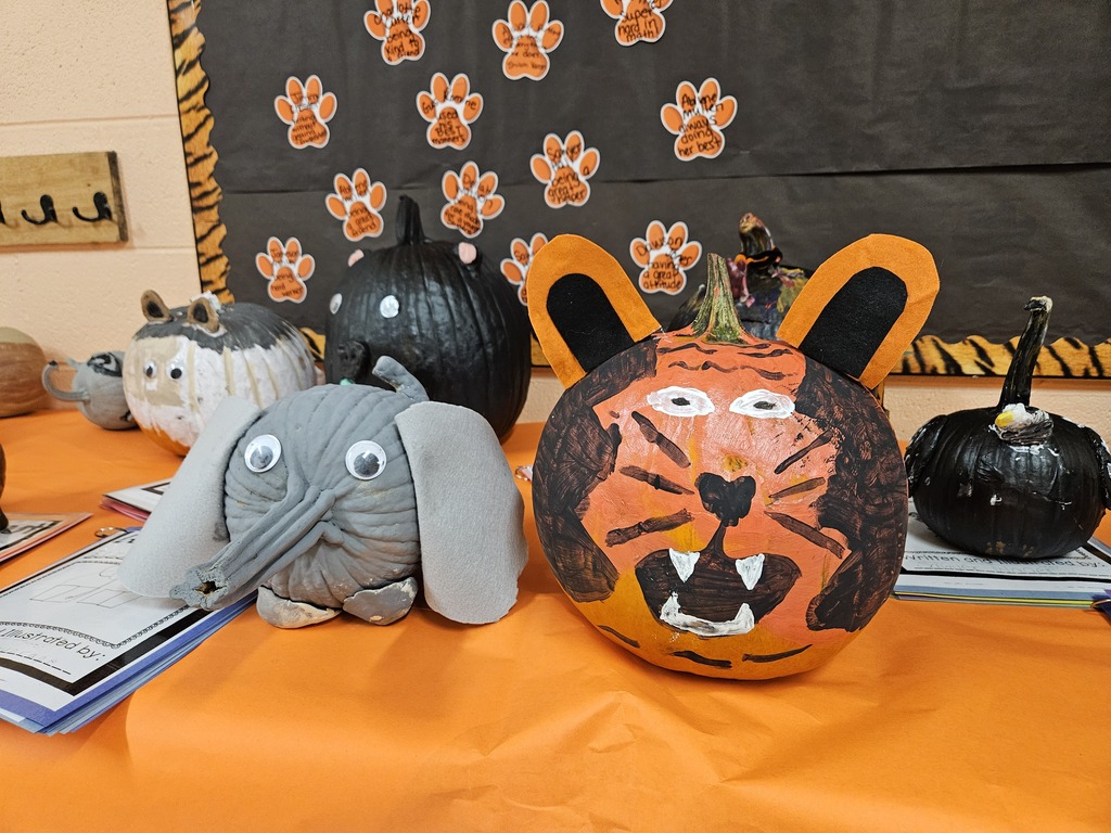 Photo showing student-created animal-themed pumpkin projects displayed in a school hallway. The pumpkins have been decorated to resemble various animals using paint and craft materials such as fabric, fur, foam pieces, and googly eyes. Each display includes a student research project about the animal represented by the pumpkin. The projects are part of a third-grade research and art activity and are exhibited on tables in the 3rd and 4th grade hallway at Wirt County Primary Center.