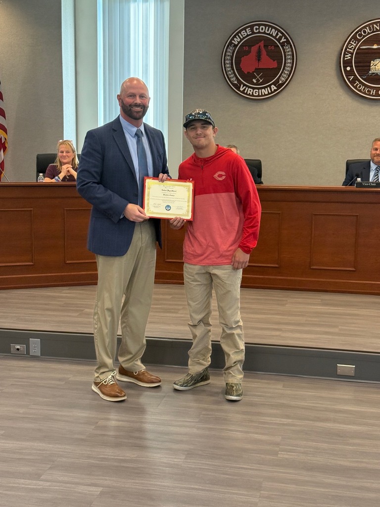 A man in a blue suit presents an award to another man in a red shirt in a courtroom.