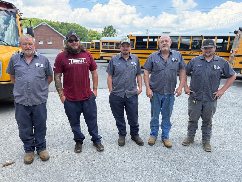 Five men stand in front of a line of yellow school buses in a parking lot.