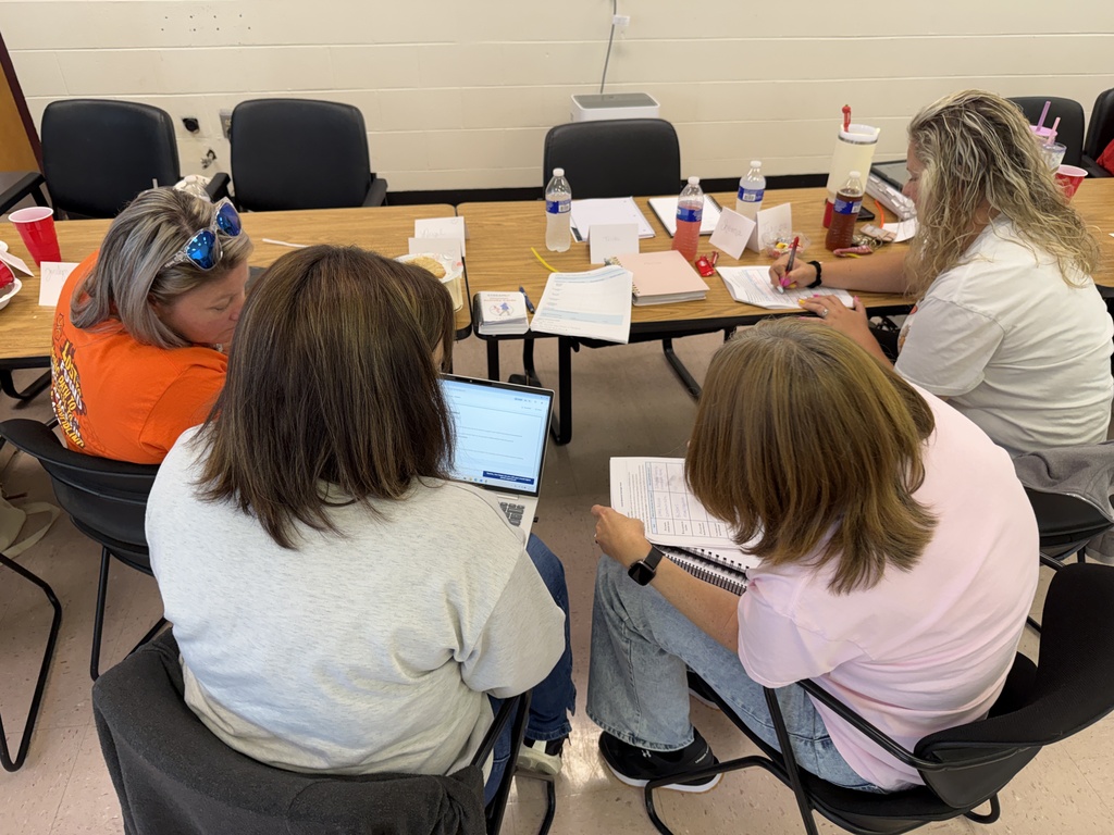 Four people sit at a table with laptops and papers. One person has sunglasses on their head.