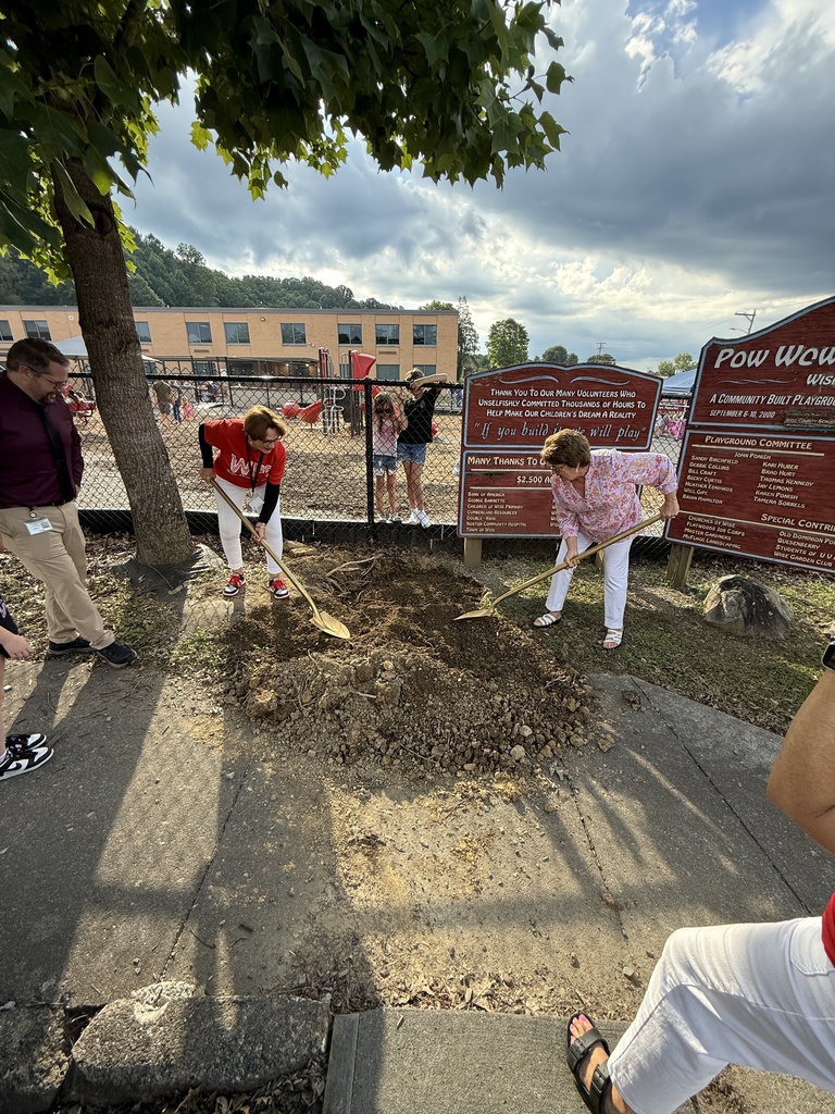 Several people are planting in the ground outside, near a fence and large sign.