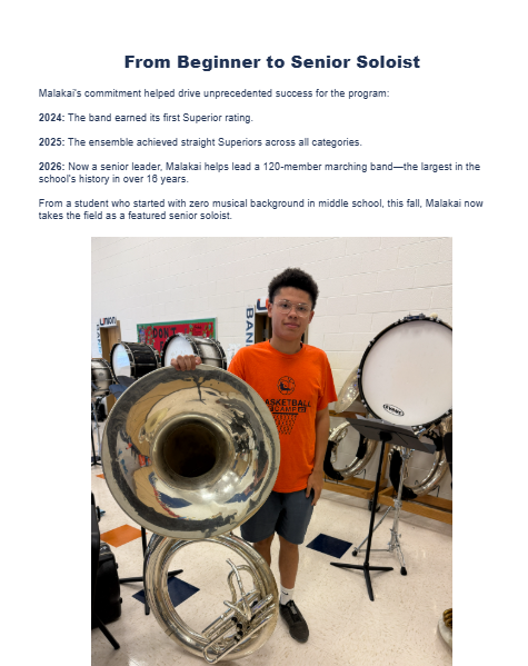 A man in an orange shirt holds a tuba, standing in a room with a drum set and other musical instruments.