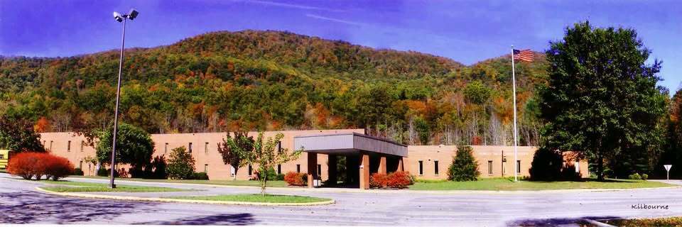 A large building with a parking lot in front. Trees and plants surround the building. Mountains in the background.