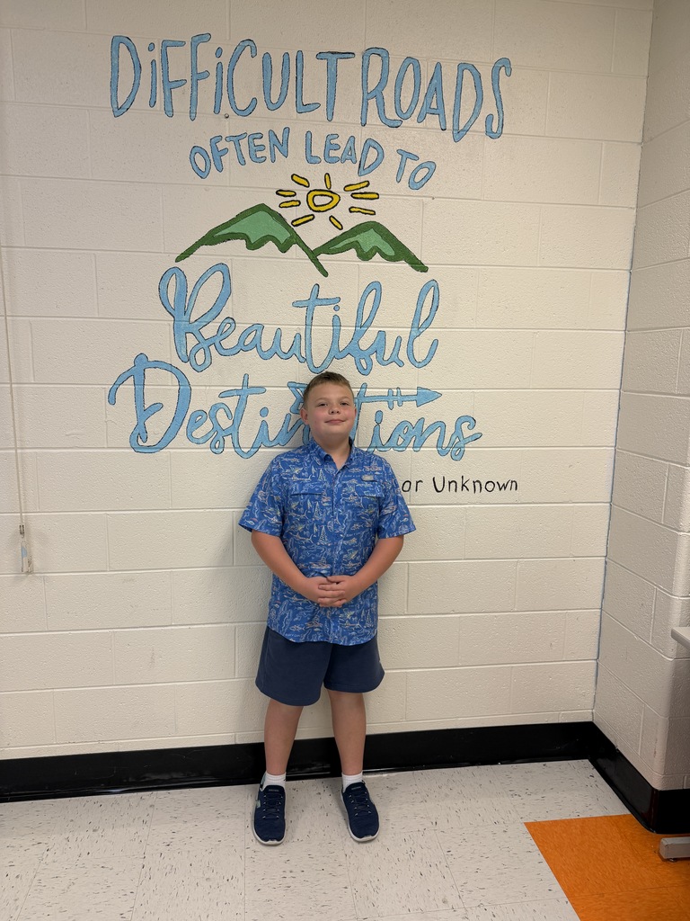A young boy in a blue shirt and black shorts stands in a hallway with a motivational wall mural.