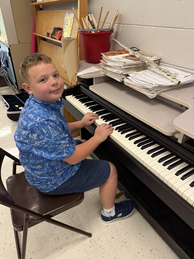 A young boy sits on a chair playing the piano with his hands on the keys.