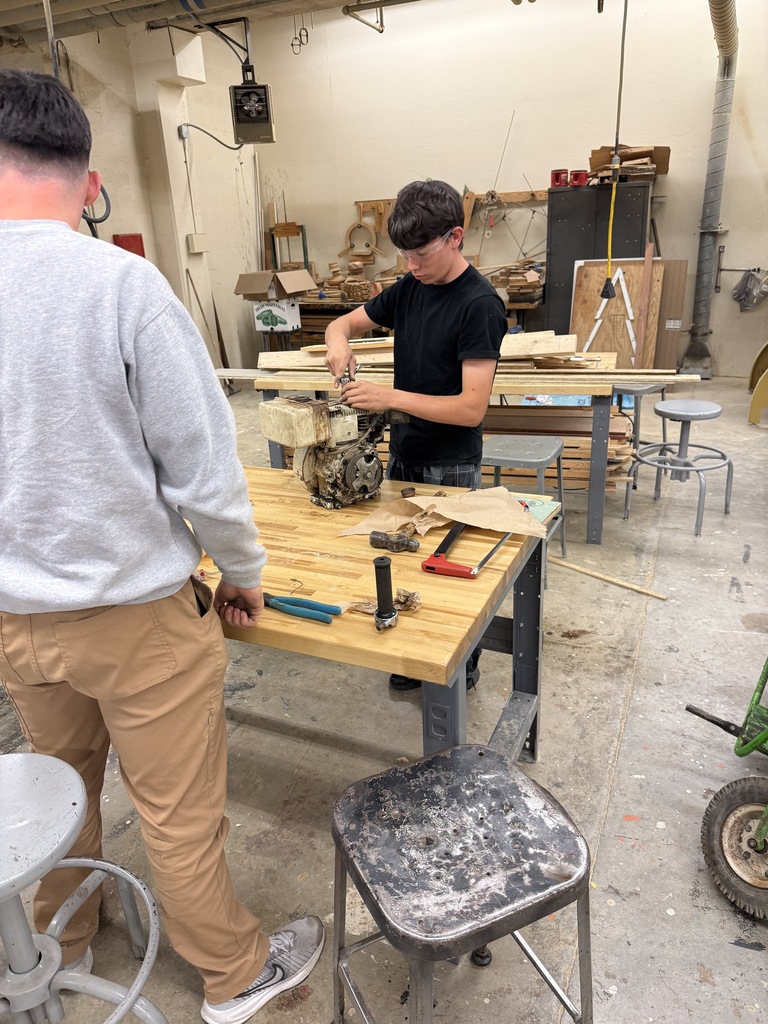 Two men in a workshop are working on a project. One man is hammering on a wooden table.