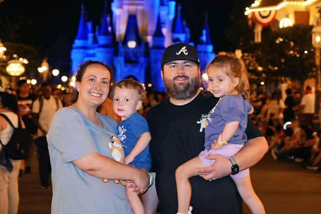Family of four, two adults and two children, posing for photo with castle in background.