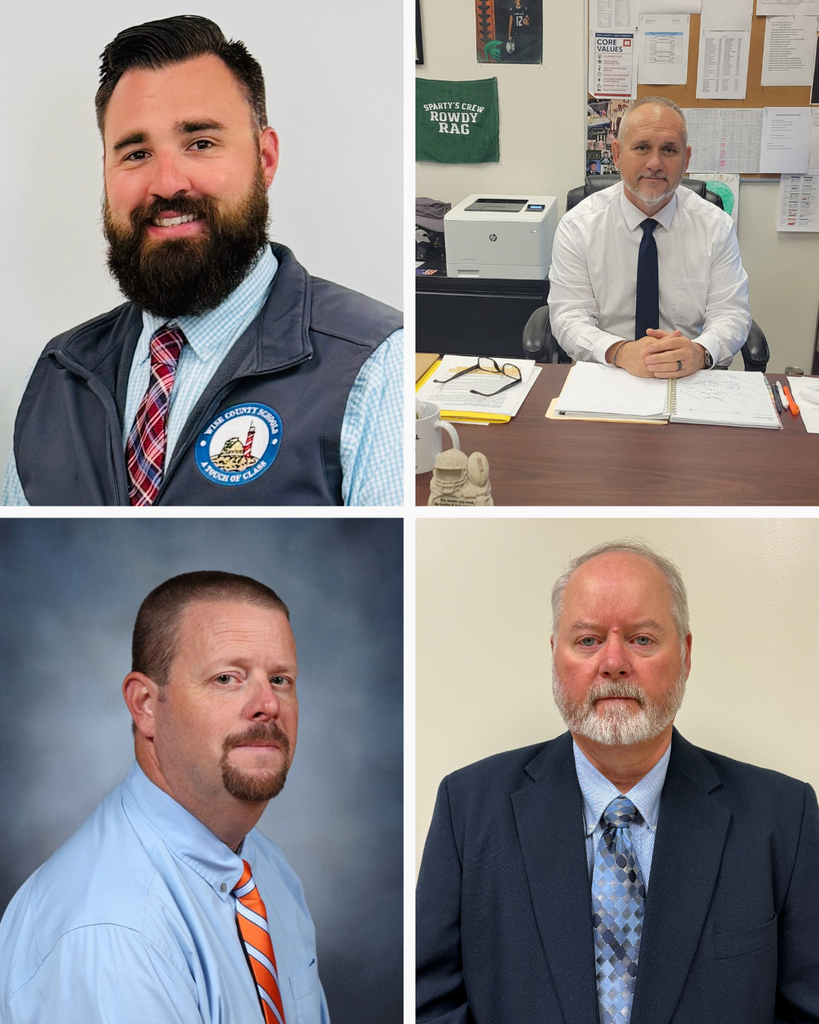 Four men in office attire: two wear ties, one with a badge; two seated, one with papers; one stands in front of a wall with bulletin board.