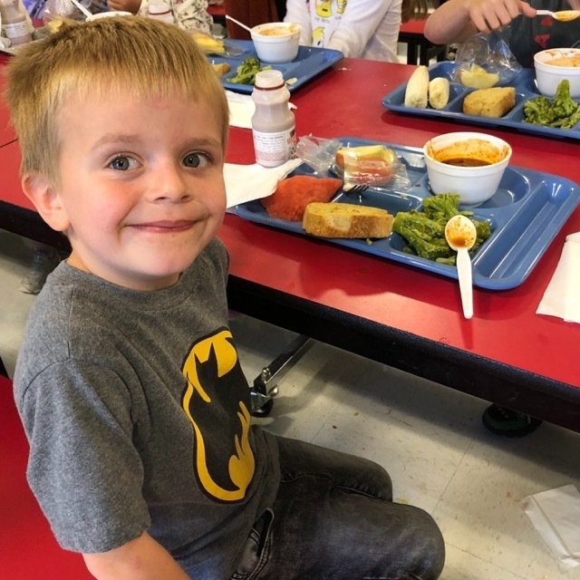 smiling child with a school lunch sitting at a table