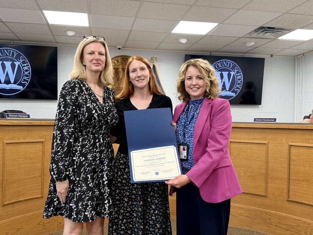 three women standing with one in the center holding a certificate